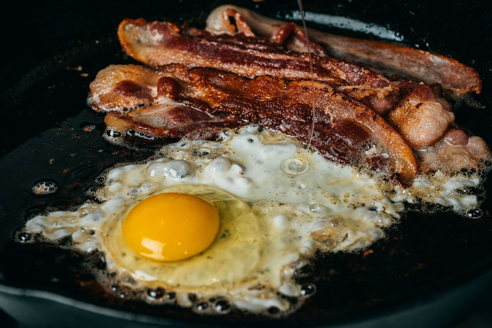 Eggs and bacon are being cooked in a skillet.