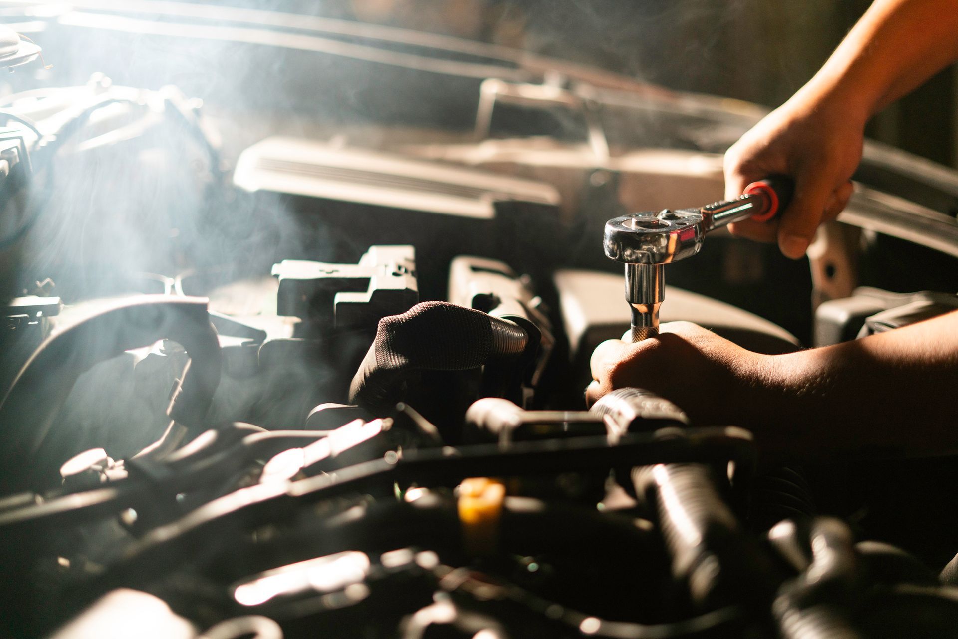 A person is working on a car engine with a wrench.