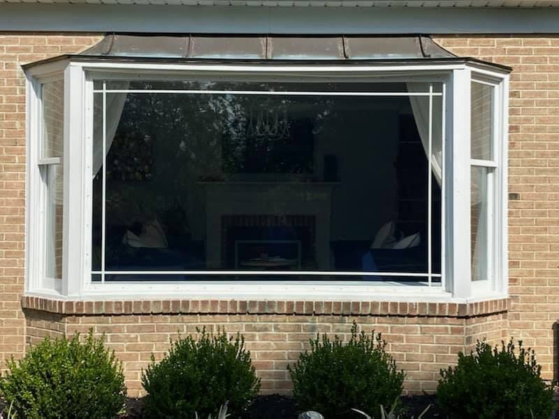 Large brick house window with white shutters and dark interior, above trimmed green shrubs