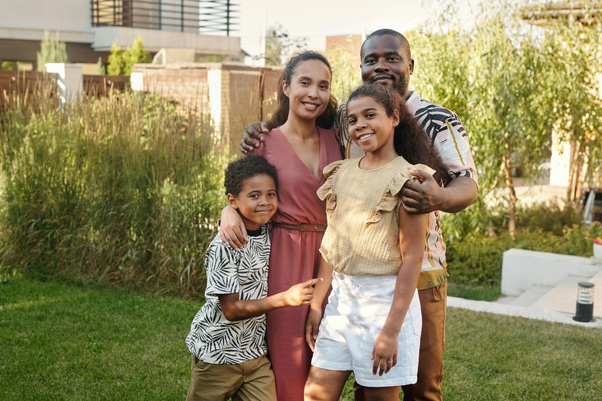 Family of four smiling in a backyard: parents with their two children.