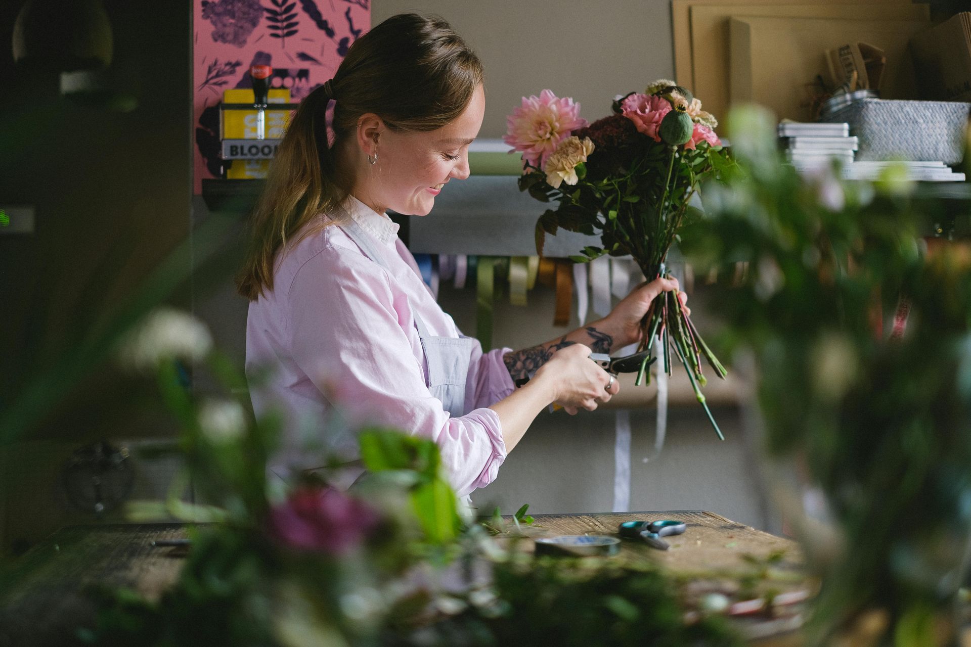 Woman in a pink shirt arranging flowers in a shop; cutting stems with scissors.