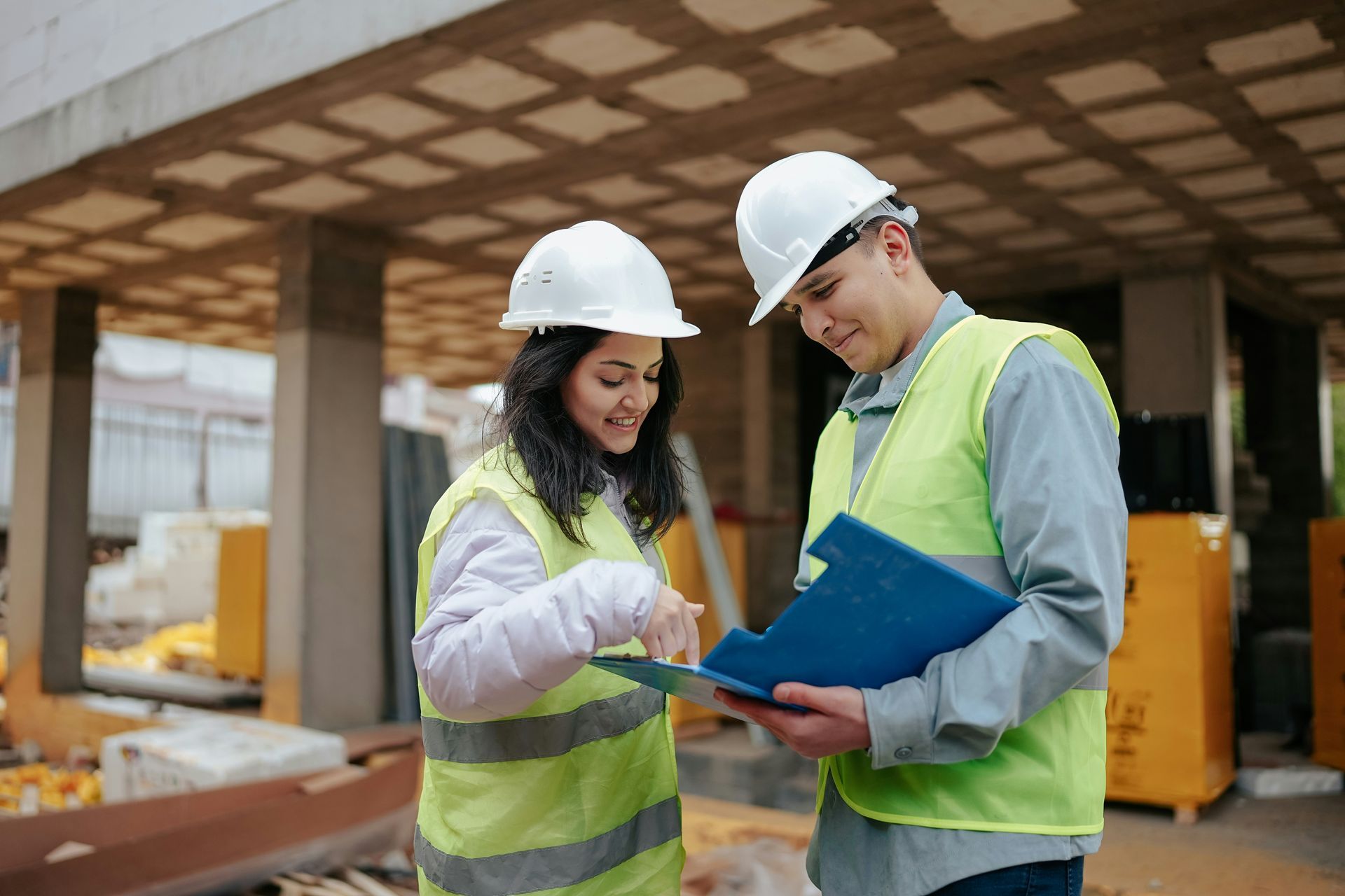 Two construction workers reviewing a blueprint on a building site, wearing safety vests and hard hats.
