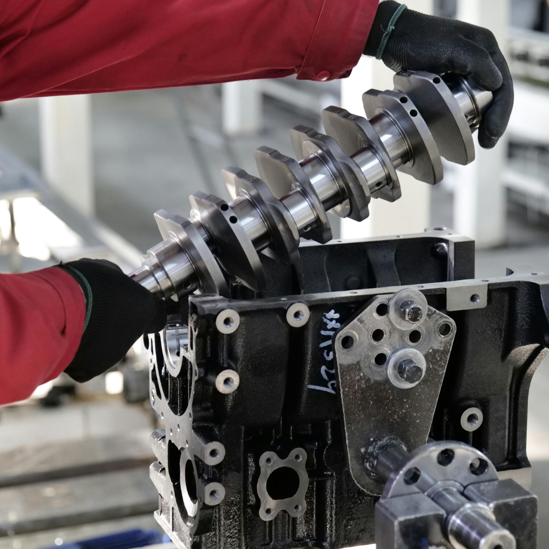 Person in black gloves installing a crankshaft into an engine block. Red sleeves are visible.