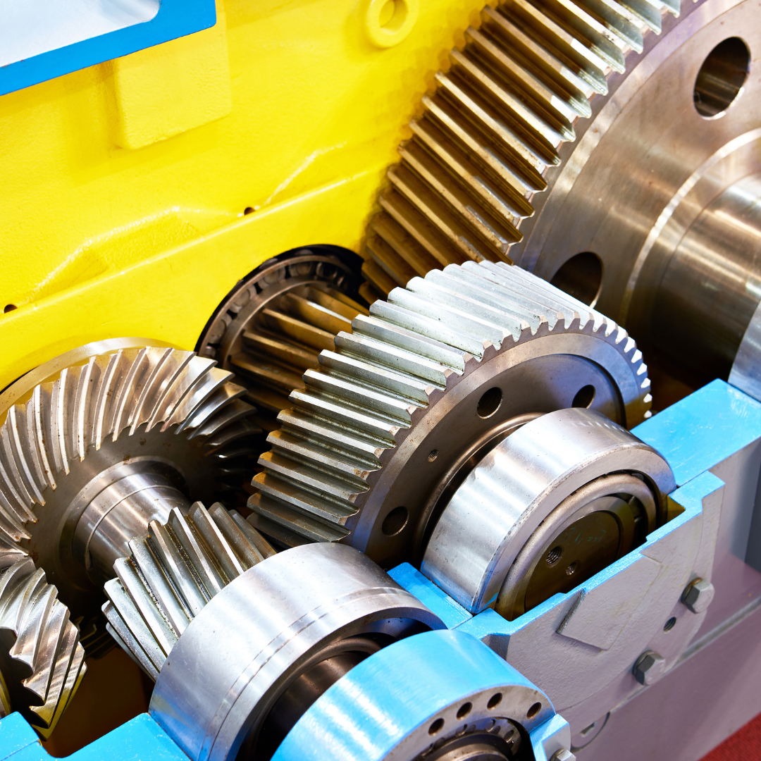 Close-up of industrial gears meshing together within a yellow and blue machine.
