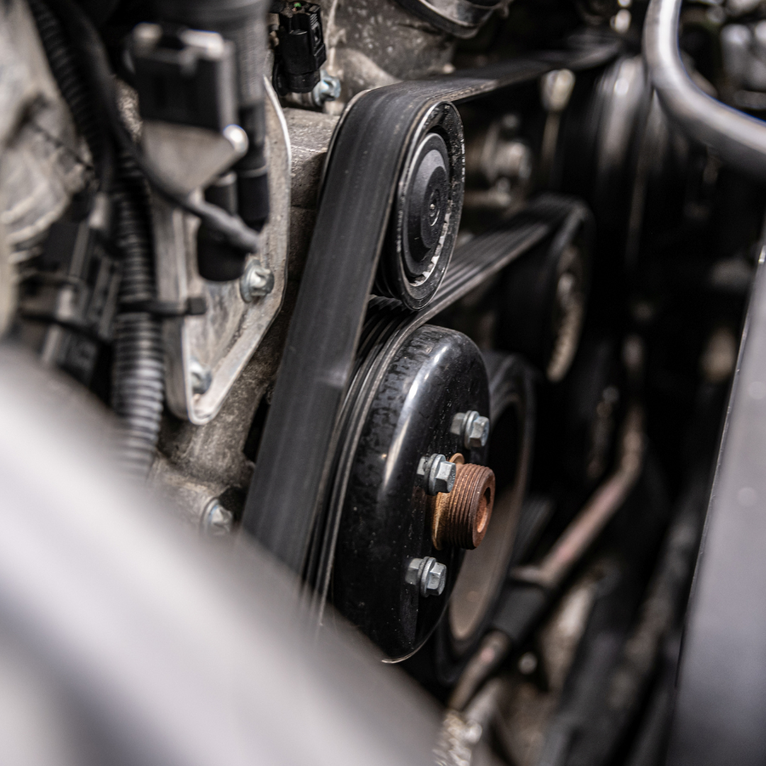 Close-up of a car engine with a serpentine belt wrapped around pulleys, in an engine bay.