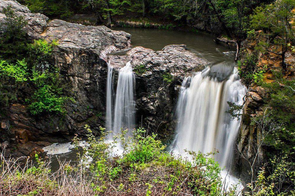 Two white waterfalls tumbling over rocky cliffs into a forest stream