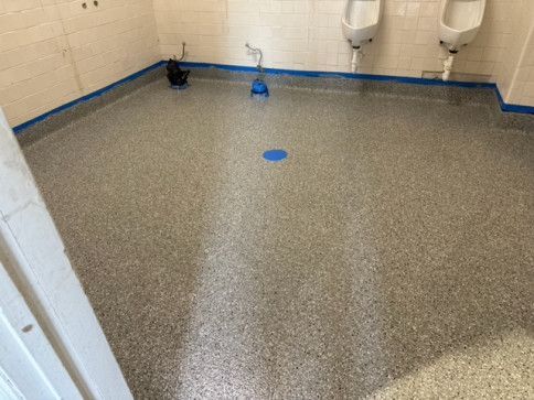A bathroom with a concrete floor and urinals on the wall.