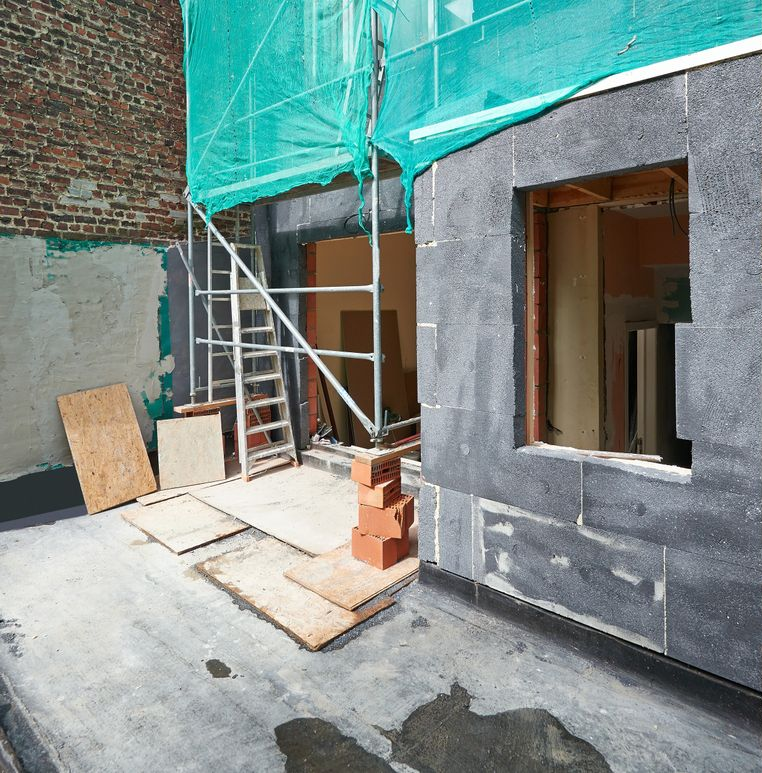 Scaffolded building exterior under renovation with ladder, green netting, and construction materials on concrete