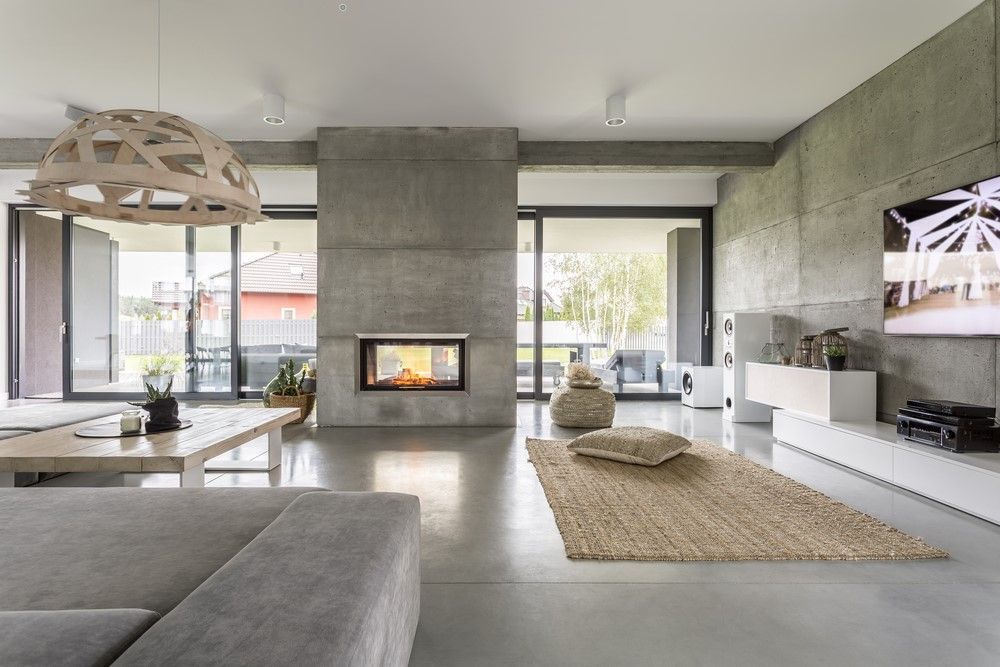 Modern minimalist living room with a fireplace, gray sofa, woven rug, and large windows