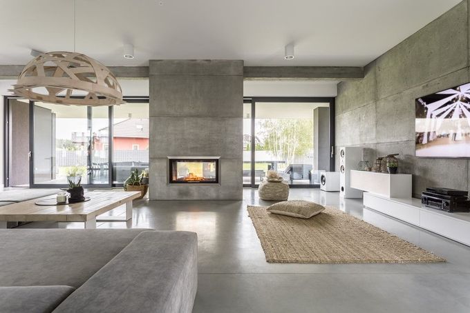Modern living room with concrete fireplace, large windows, gray sofa, and woven pendant light