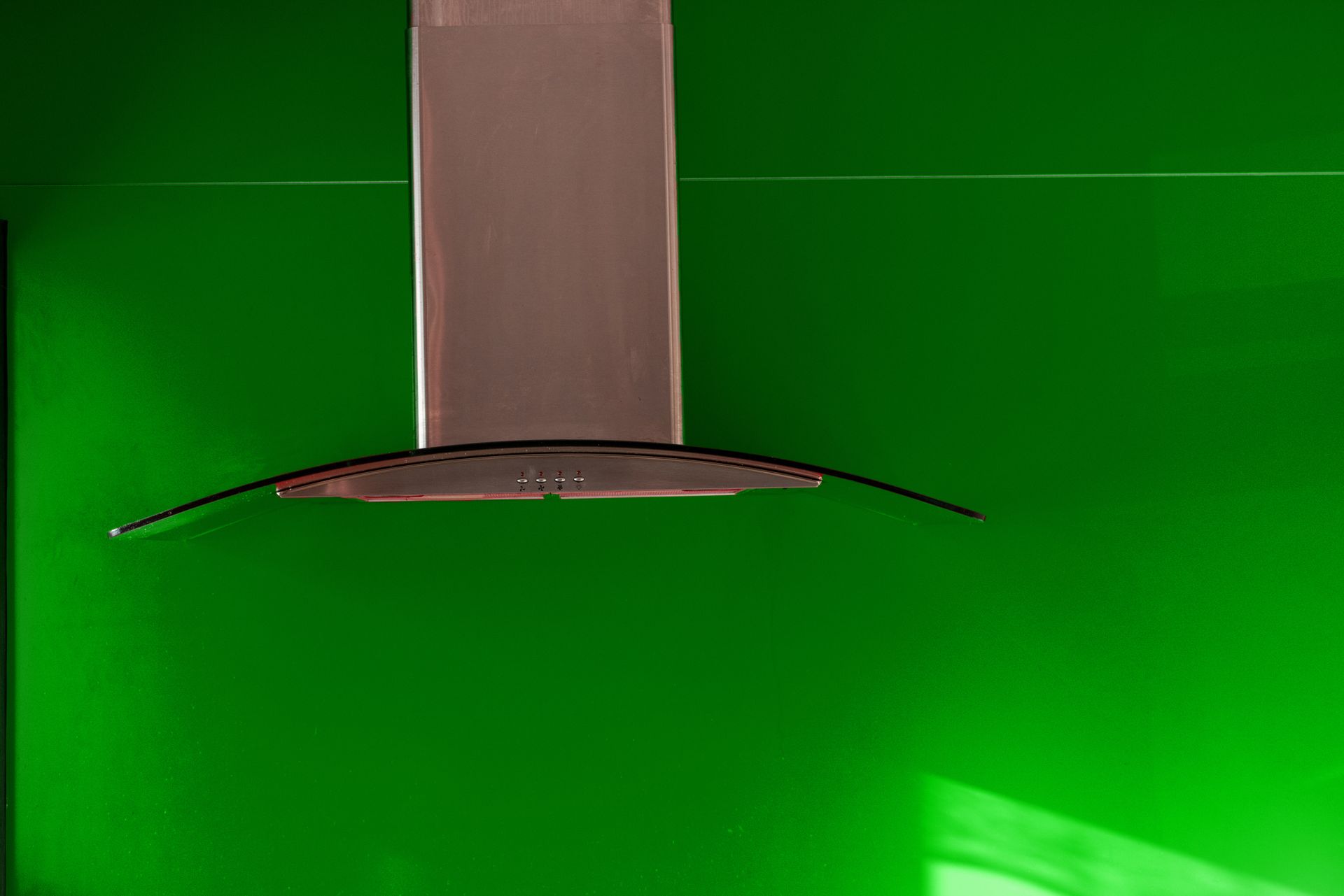 A stainless steel exhaust hood is hanging from the ceiling in front of a green wall.