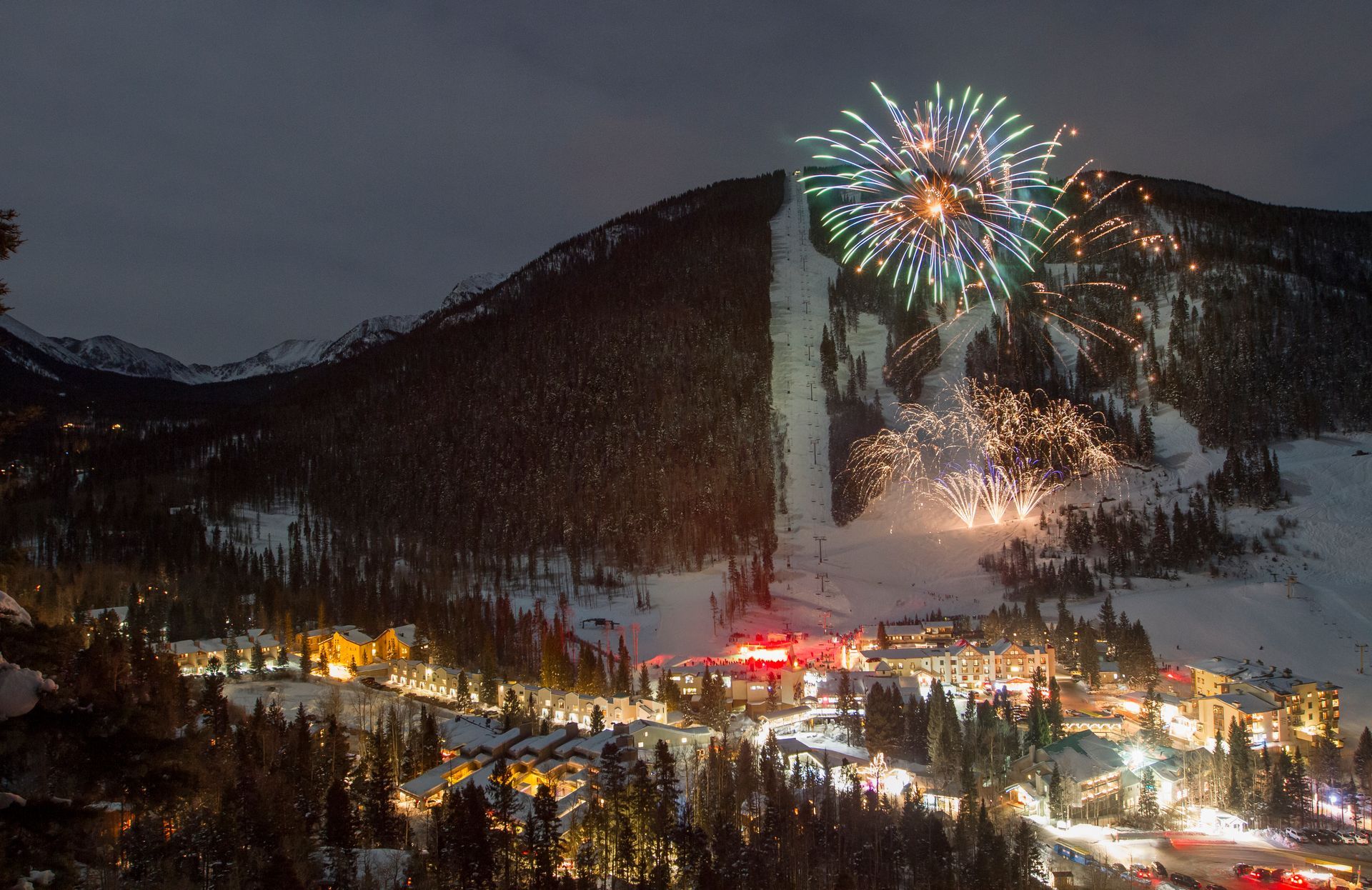 Fireworks are being displayed over a ski resort at night.