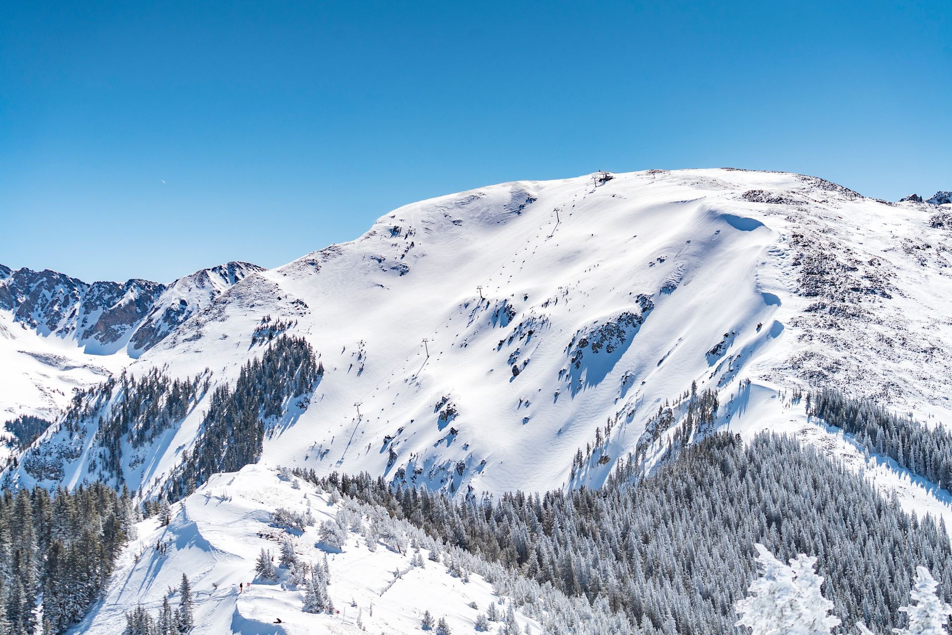 A snowy mountain with trees on the side and a blue sky in the background