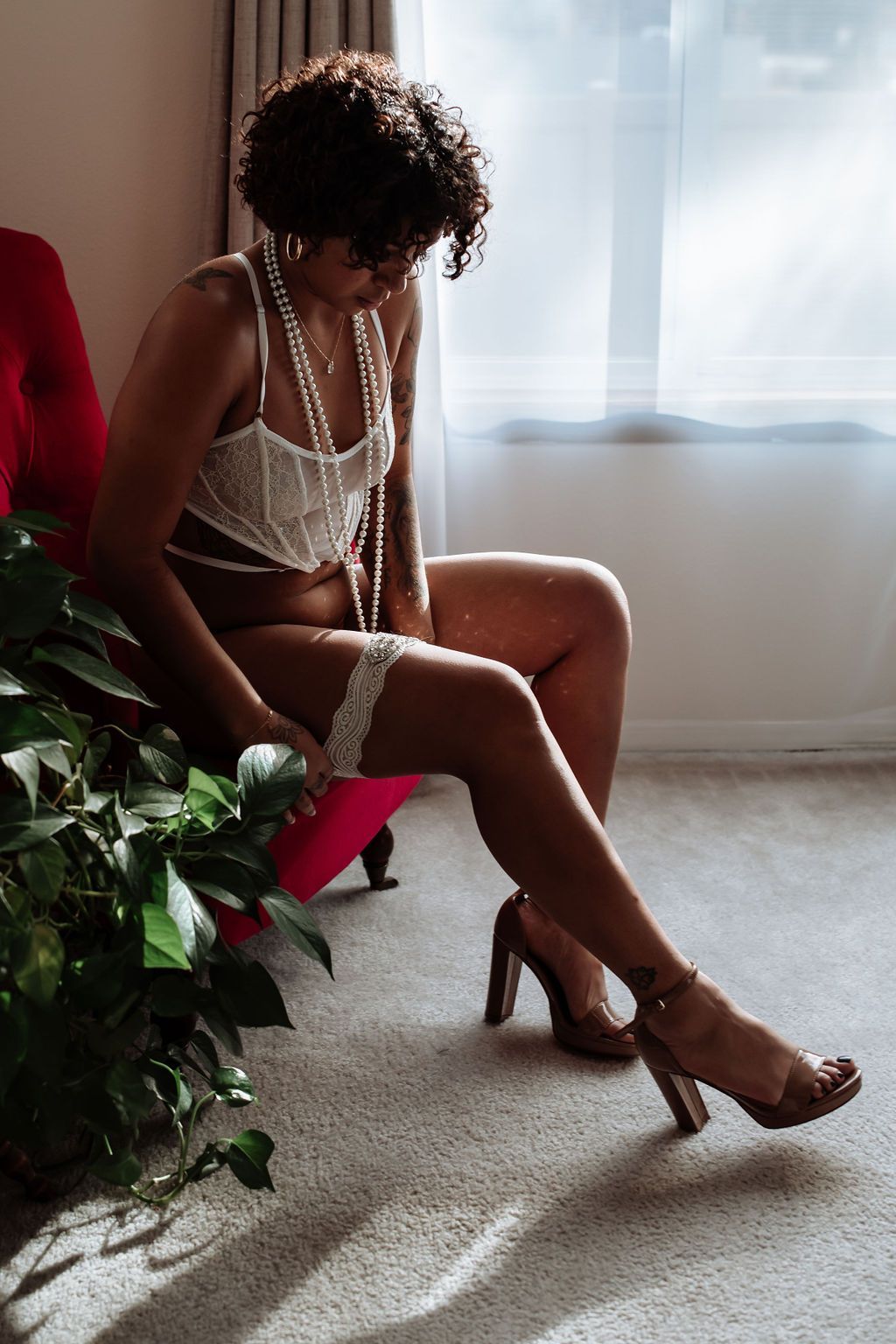 A woman in lingerie is sitting on a chair in front of a window.