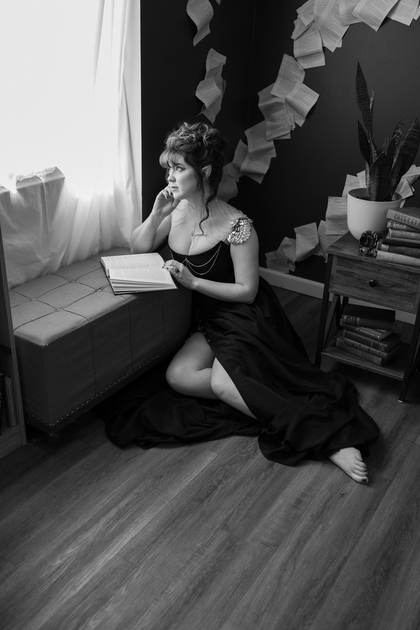 A woman in a black dress is kneeling on the floor reading a book.