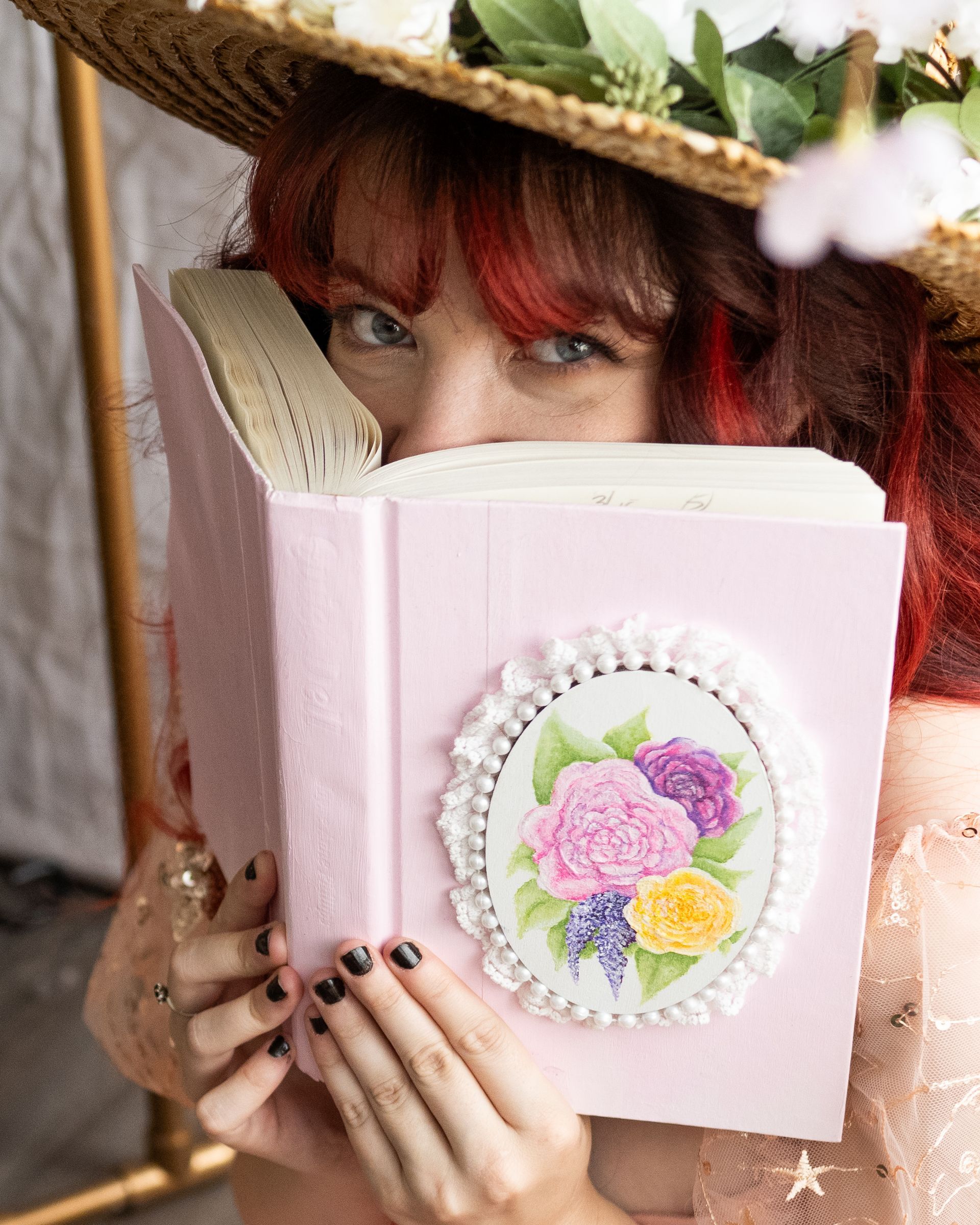 A woman in a straw hat is holding a pink book with flowers on it.