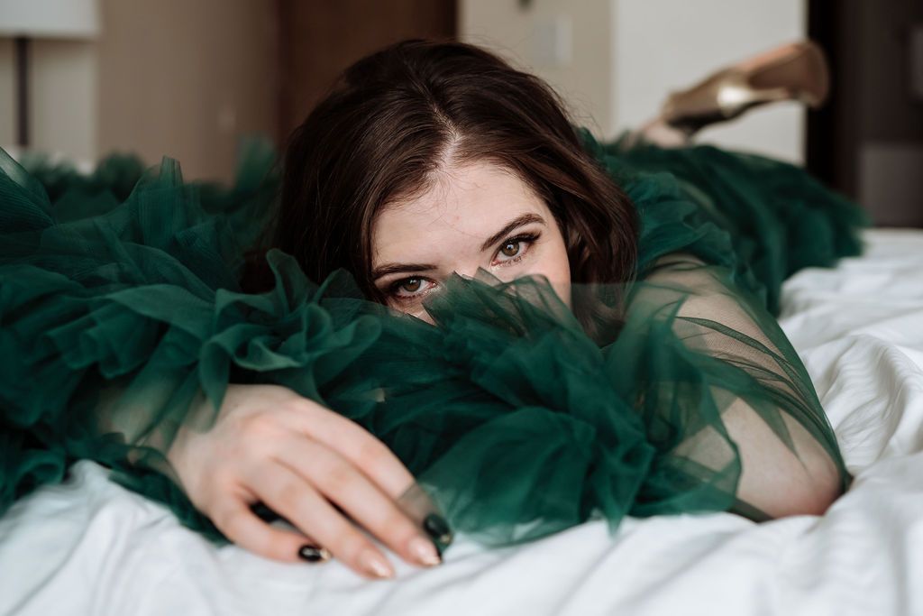 A woman in a green dress is laying on a bed.