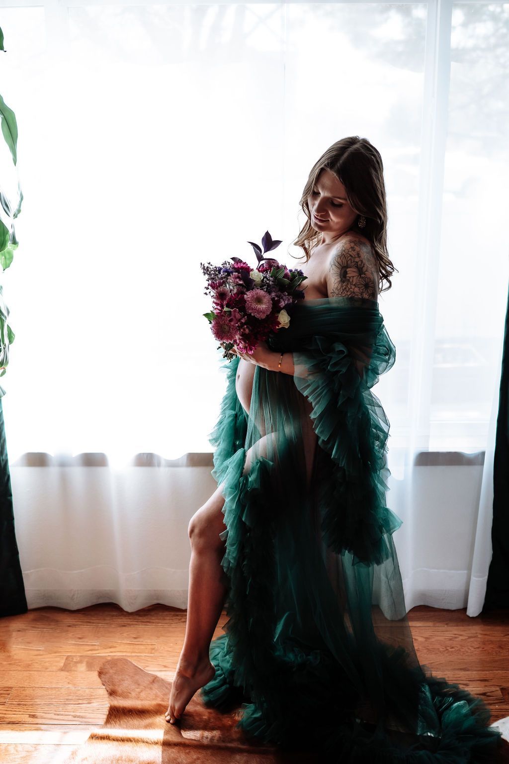 A pregnant woman in a green dress is holding a bouquet of flowers.