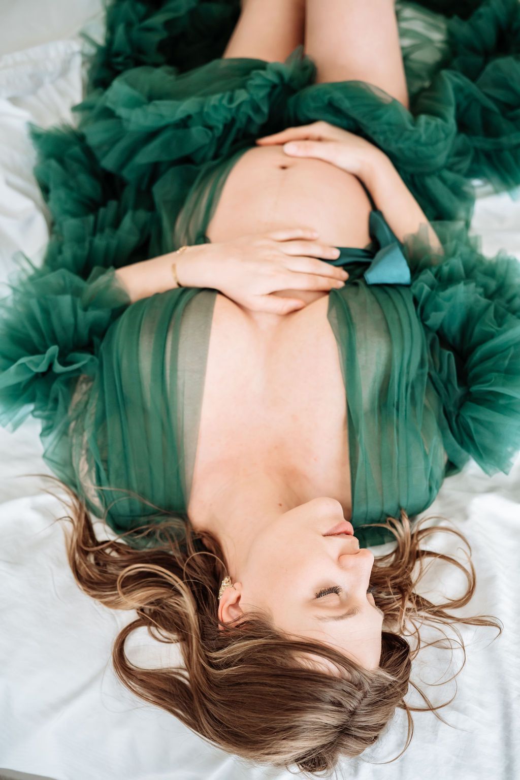 Women in green toole lingerie laying upside down on a white sheet
