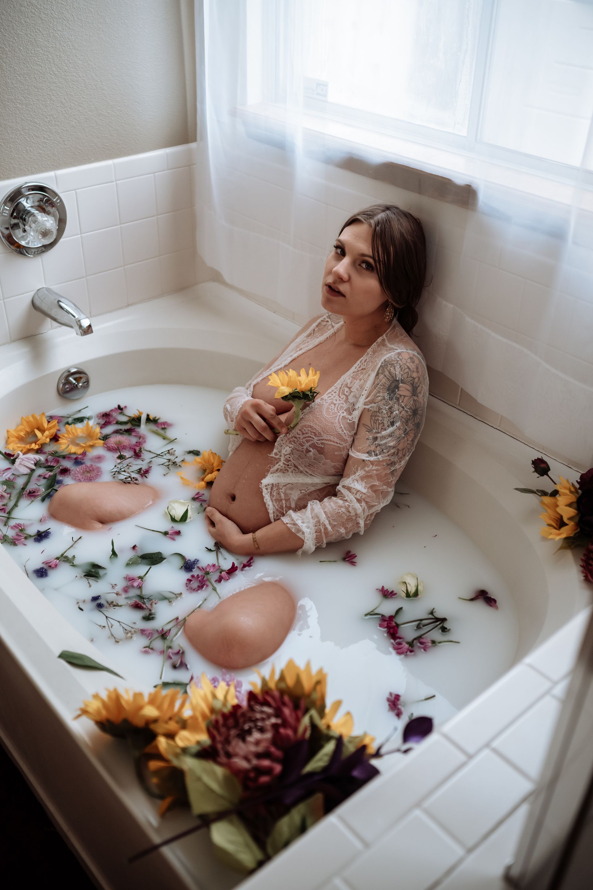 A pregnant woman is sitting in a bathtub filled with milk and flowers.