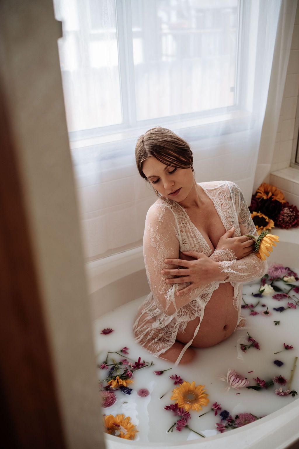 A pregnant woman is sitting in a bathtub filled with milk and flowers.