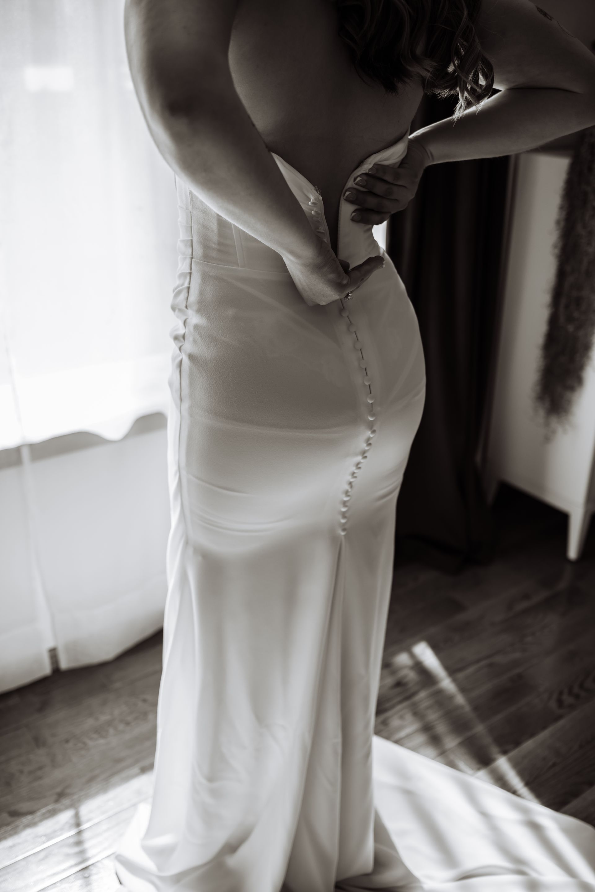 A woman is putting on her wedding dress in a black and white photo.