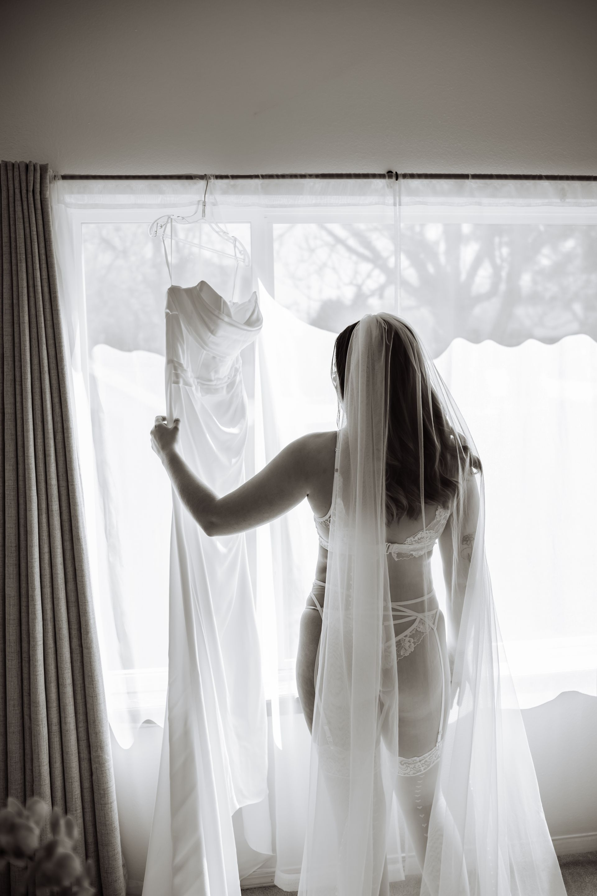 A woman in a wedding dress and veil is standing in front of a window.