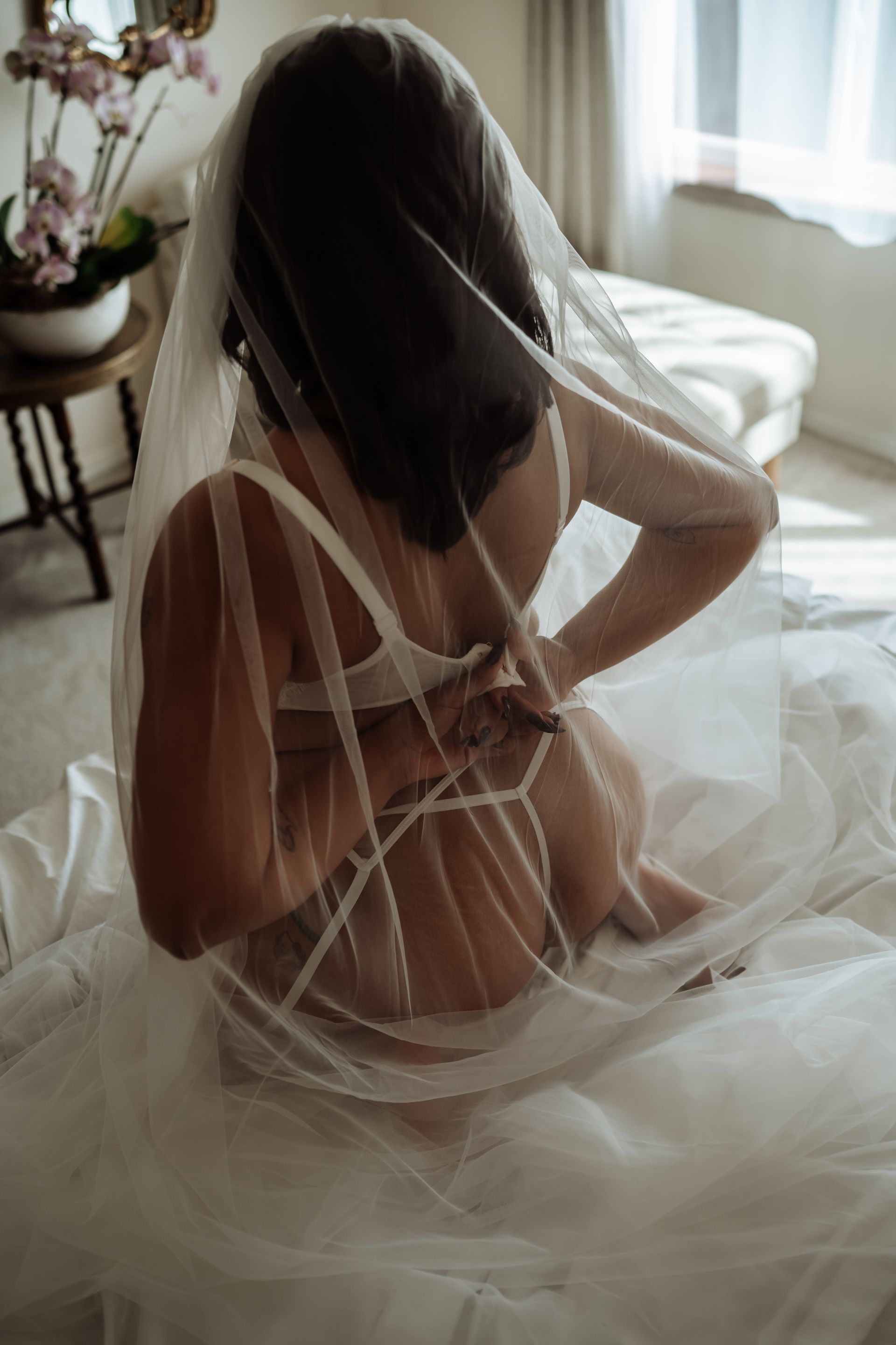 A woman in lingerie and a veil is sitting on a bed.