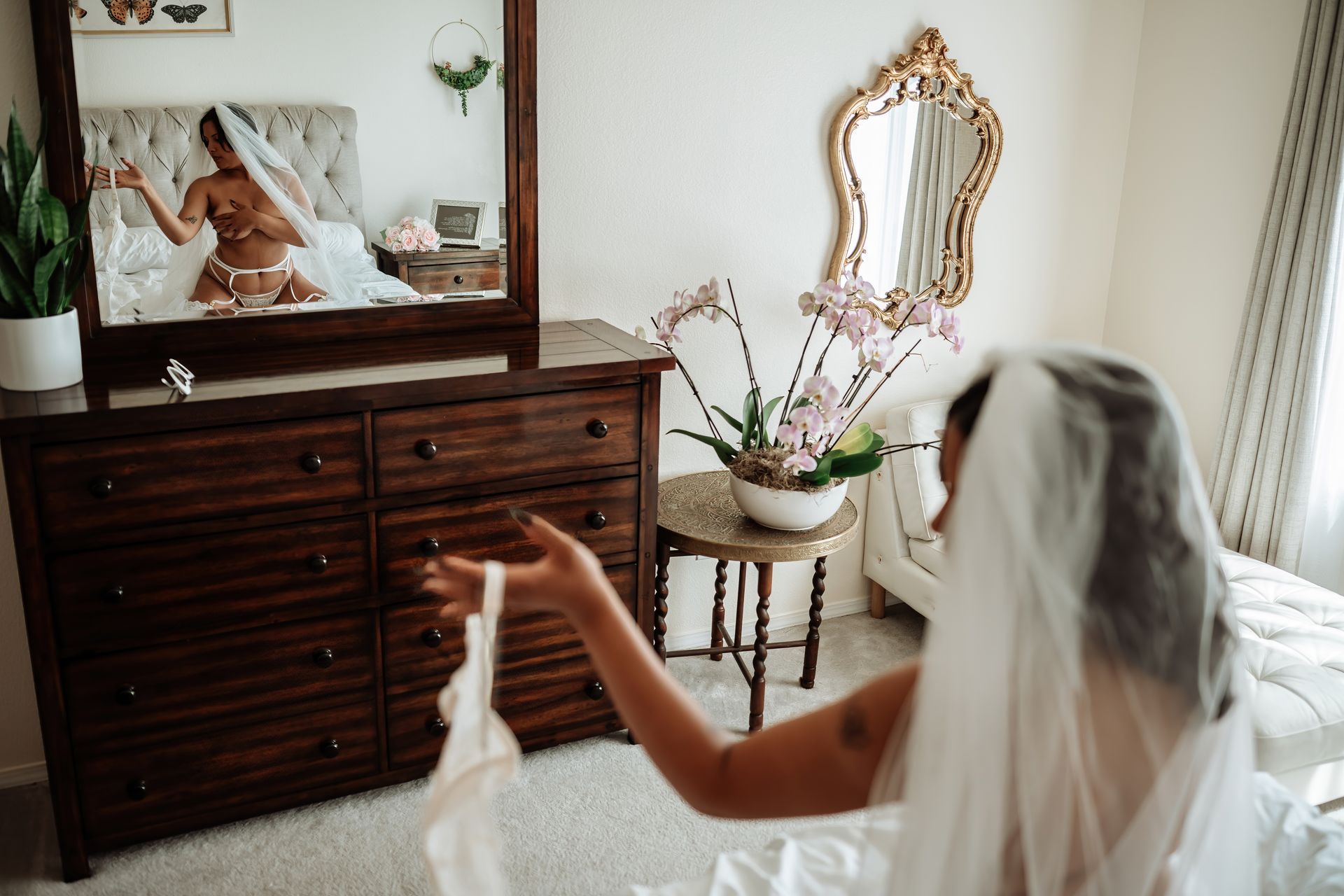 A bride in a veil is standing in front of a mirror in a bedroom.