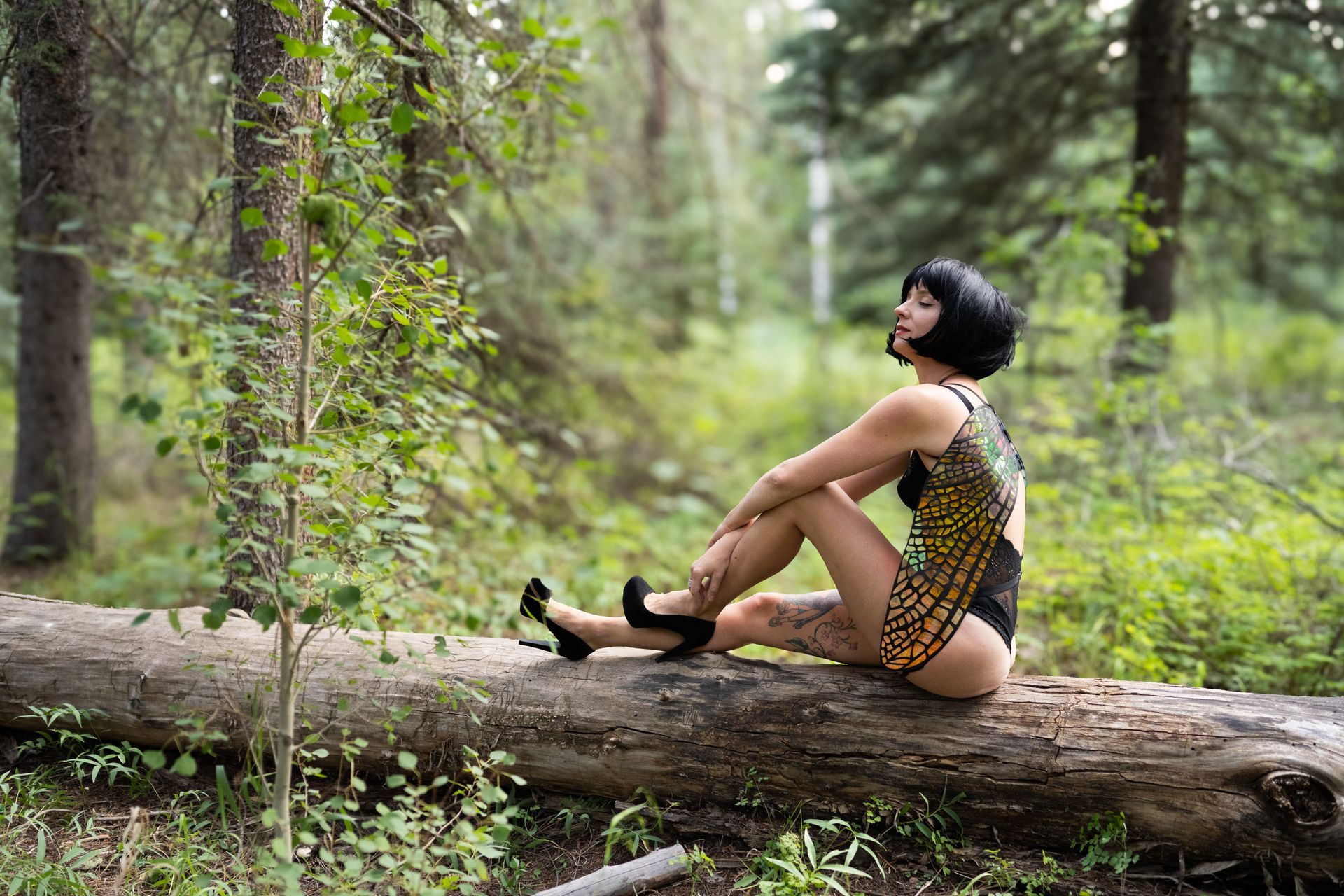 A woman in a bathing suit is sitting on a log in the woods.
