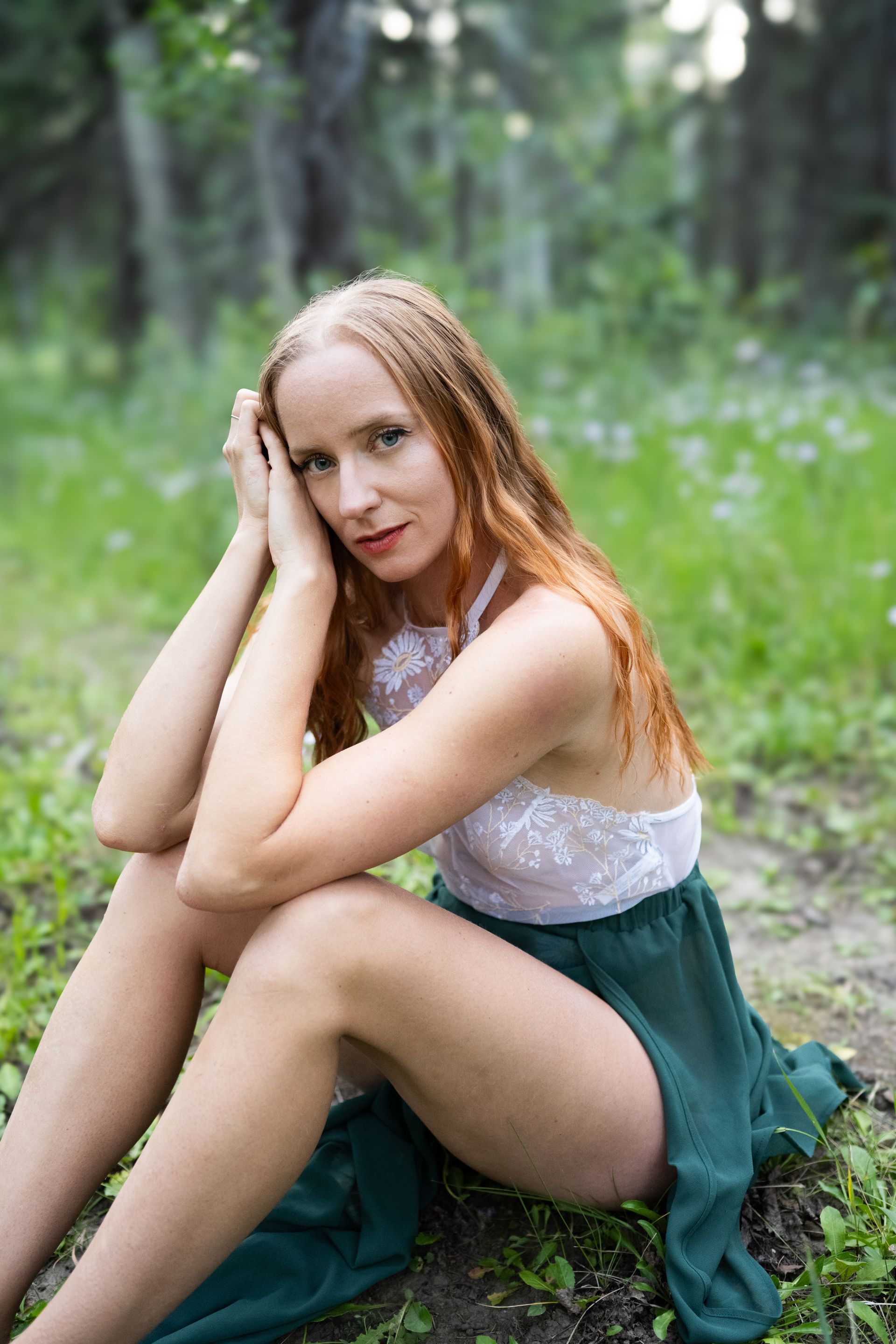 A woman sitting in long grass with flowers behind her. 