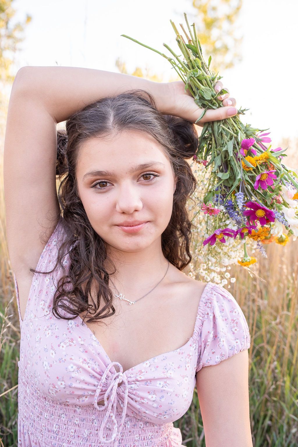 Young girl looking at the camera with her arm over her head holding dried flowers