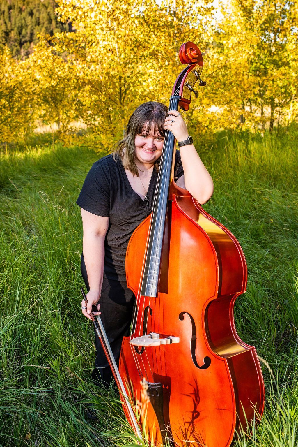 A woman is holding a double bass in a field.