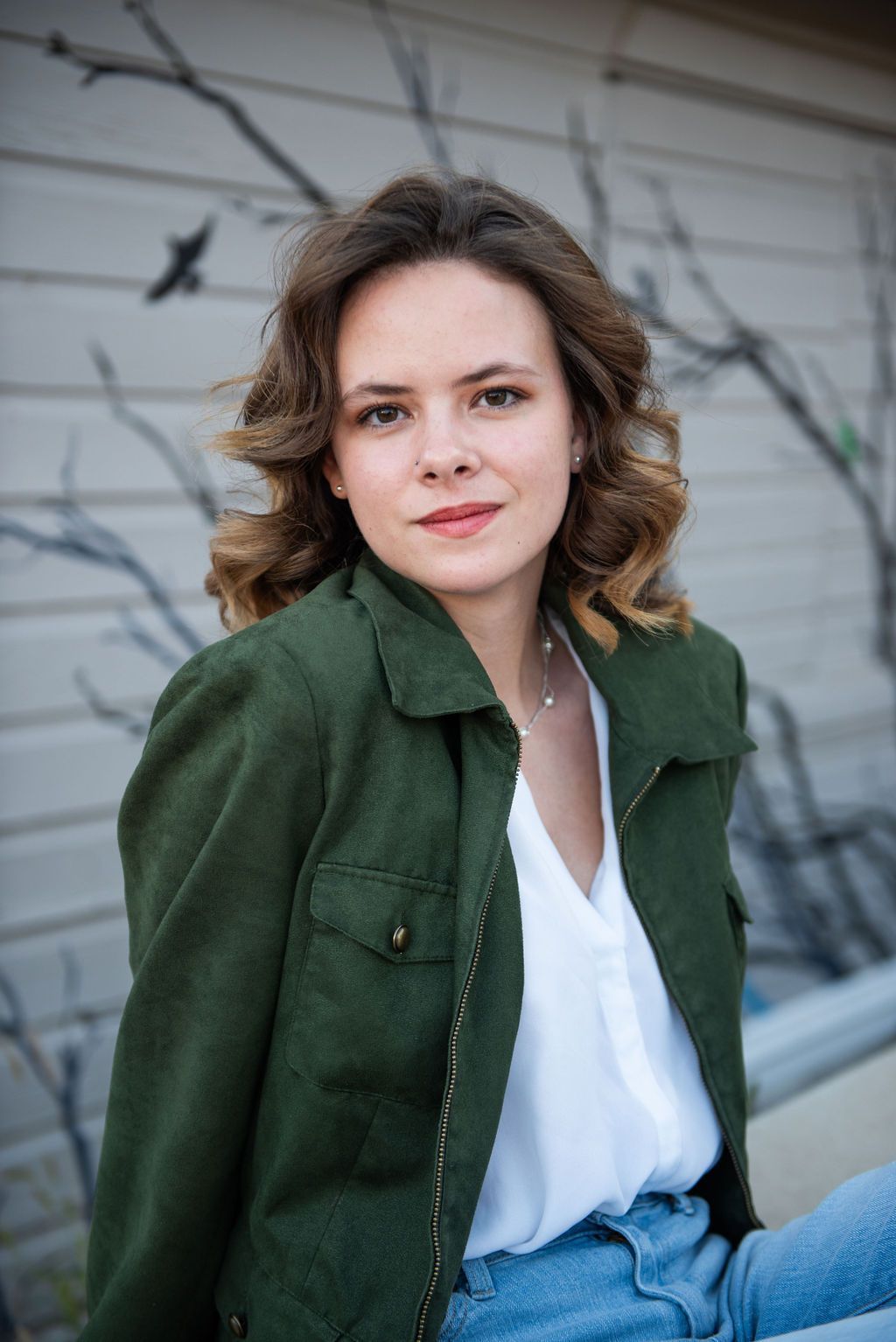 A woman wearing a green jacket and a white shirt is sitting in front of a building.