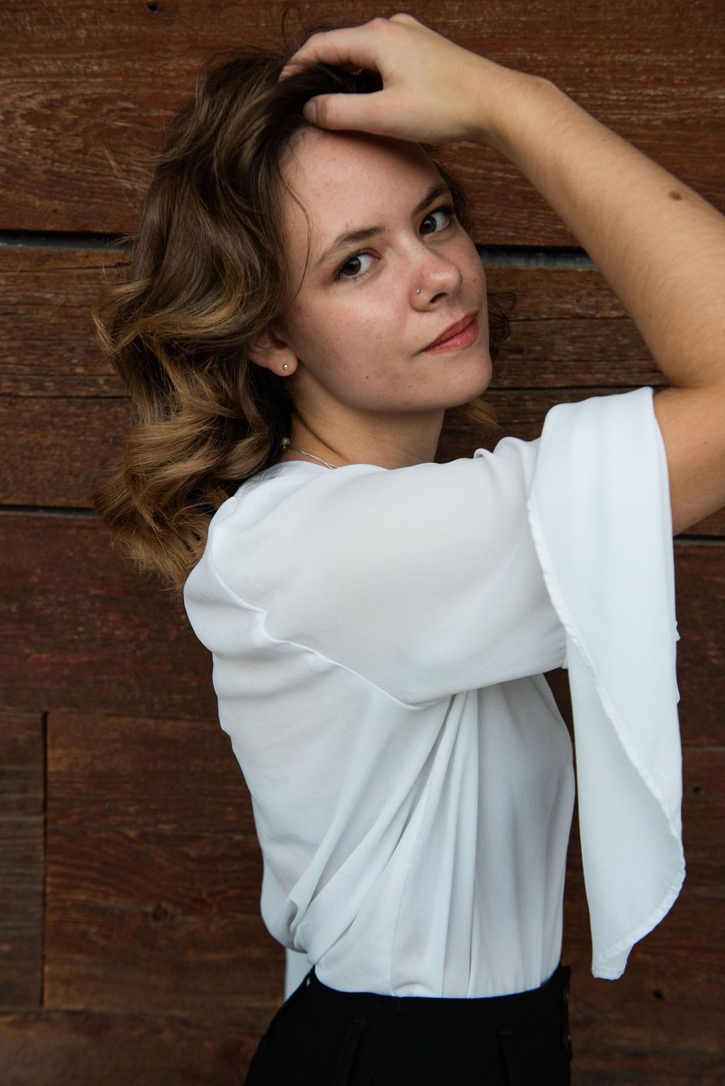 A woman in a white shirt is standing in front of a wooden wall.