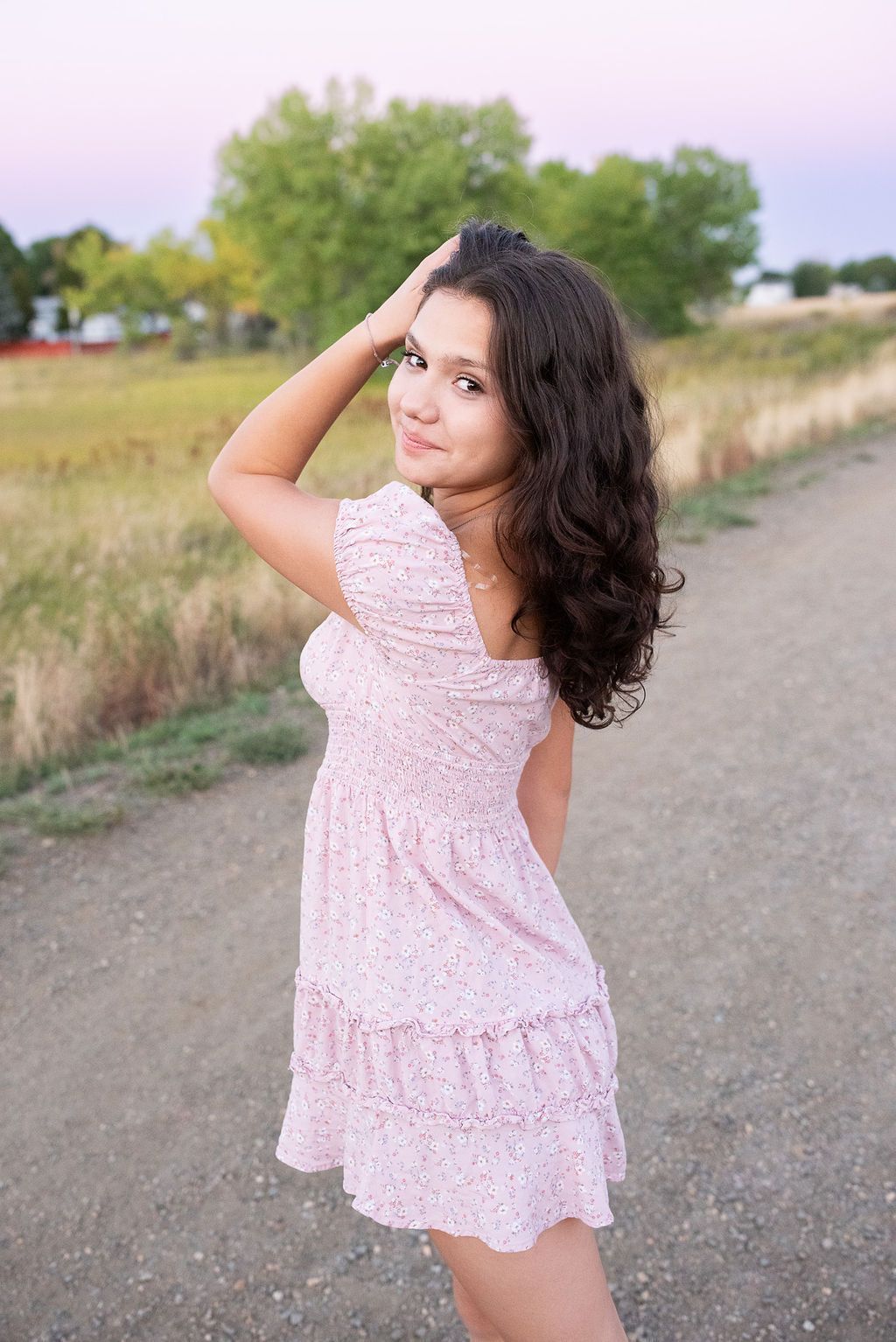 A woman in a pink dress is standing on a dirt road.