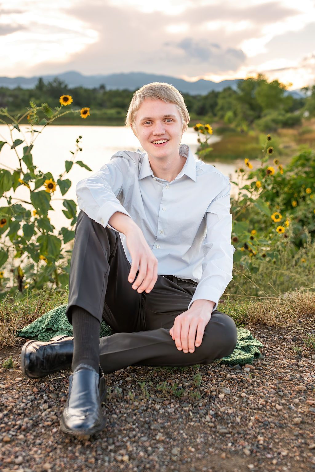 A young man is sitting on the ground in front of a lake.