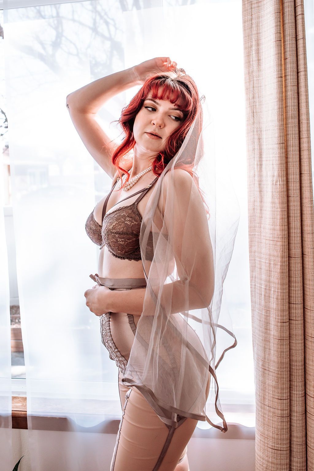 A woman in lingerie is standing in front of a window.