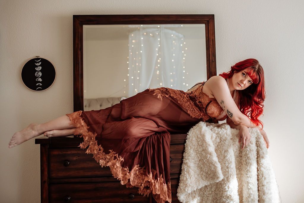 A woman in a dress is laying on a dresser in front of a mirror.