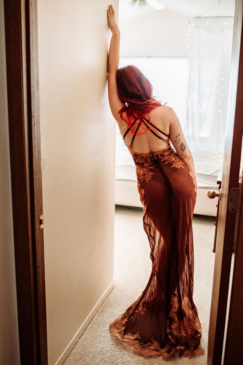 A woman in a long dress is leaning against a wall in a hallway.