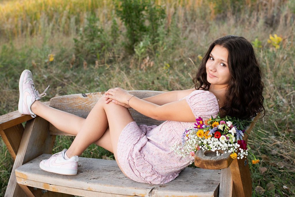 A woman in a pink dress is laying on a wooden bench with flowers in her hair.