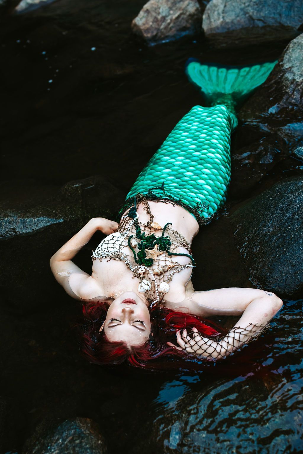 A woman dressed as a mermaid is laying on her back in the water.