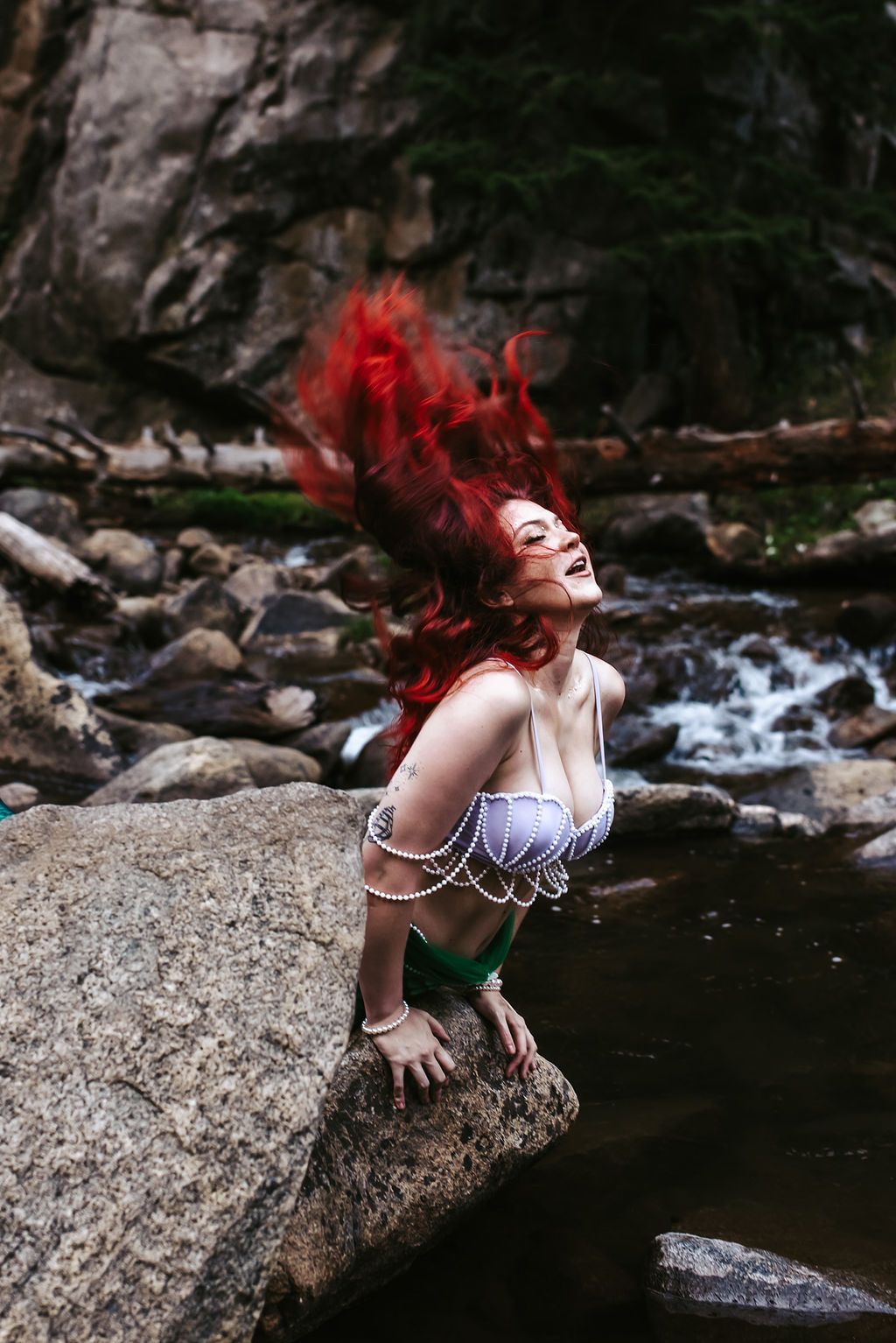 A woman in a mermaid costume is sitting on a rock in the water.