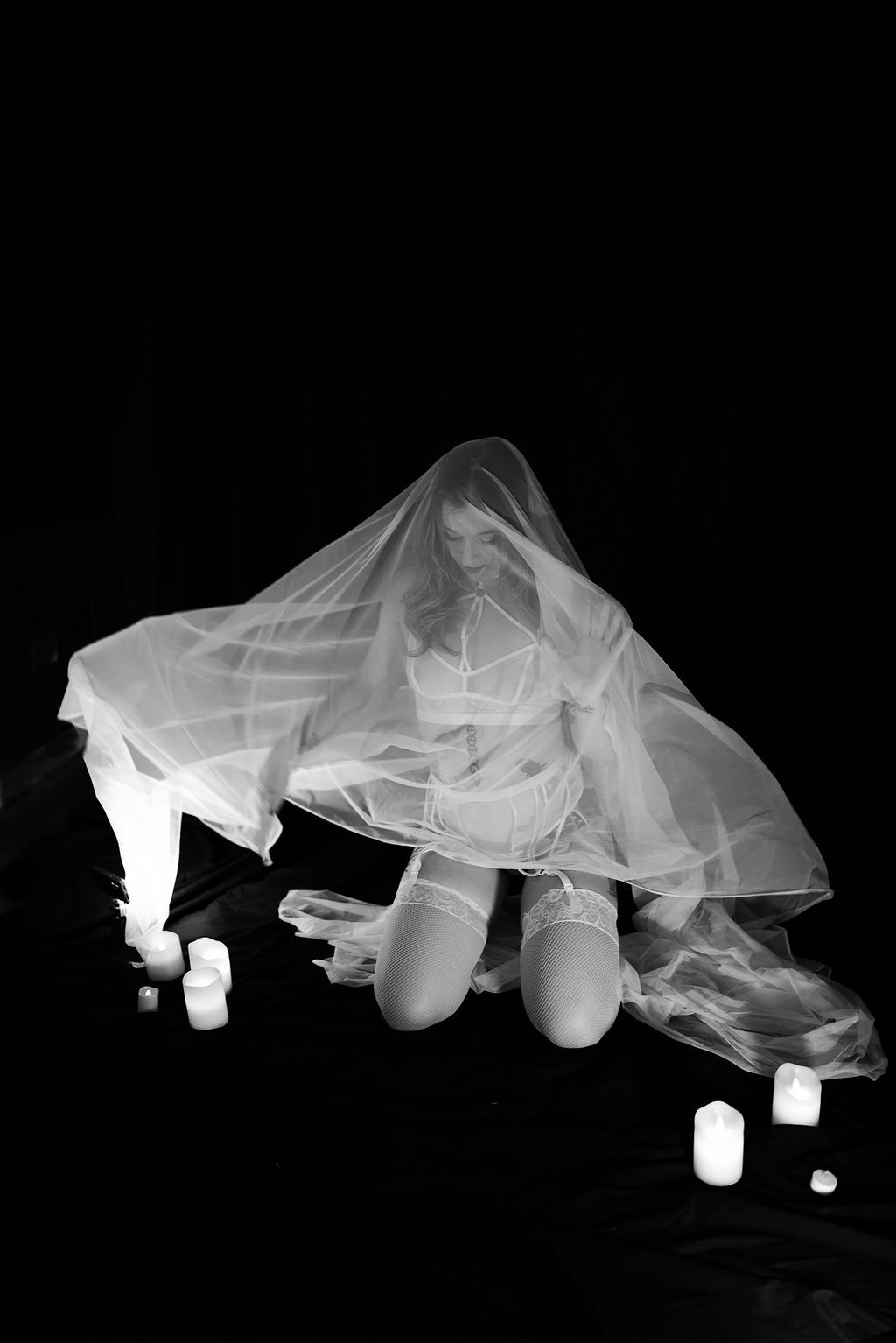 A woman in a white veil is kneeling down in front of candles.