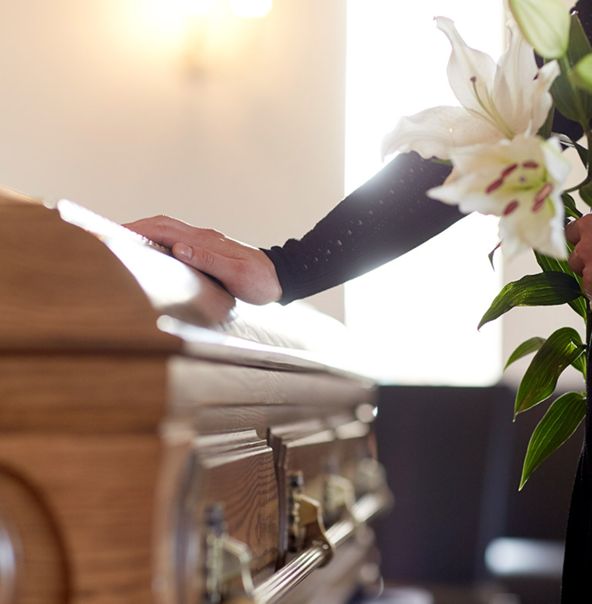 A woman is standing next to a coffin with flowers in front of it.