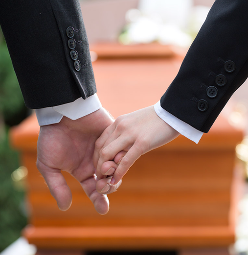 A man and woman are holding hands in front of a coffin