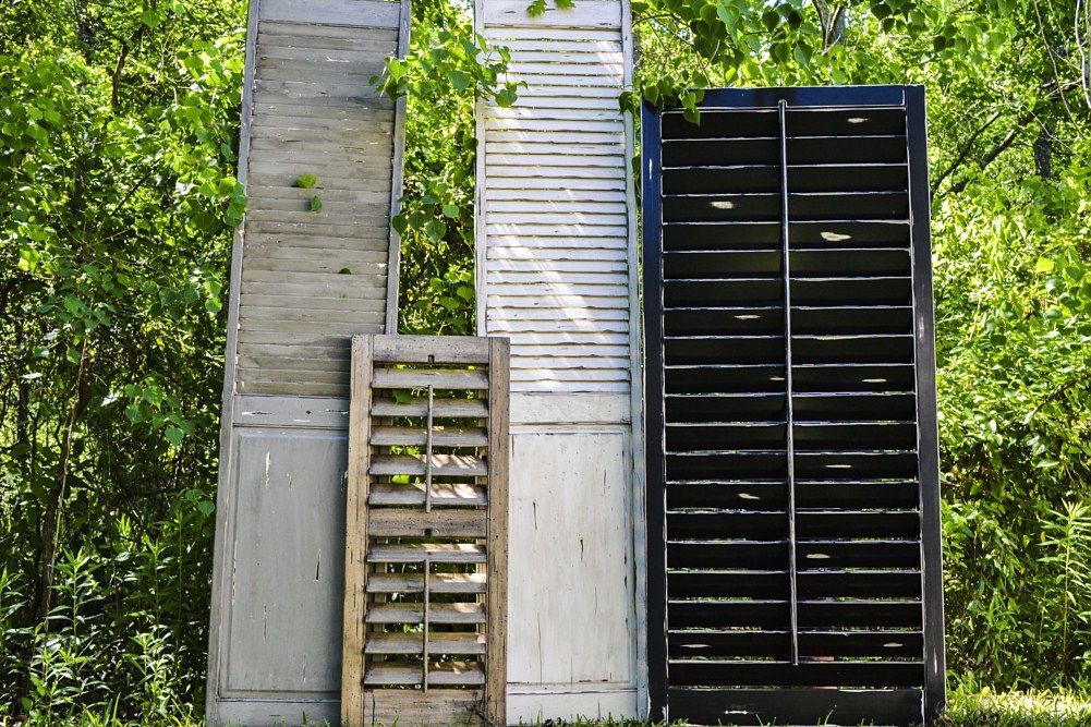 Three shutters are stacked on top of each other in front of trees