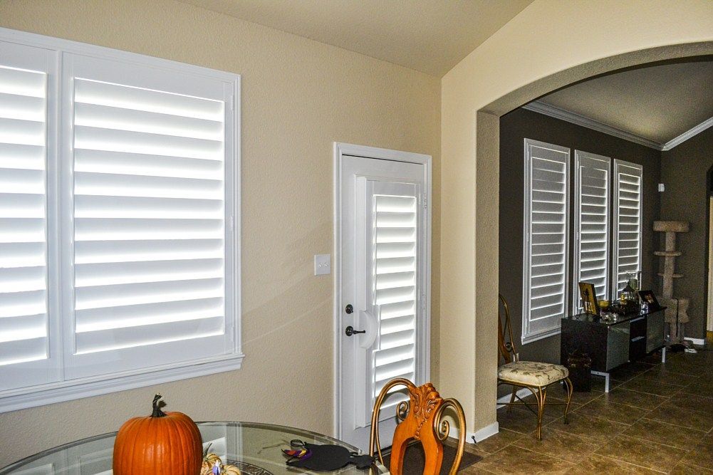 A living room with a pumpkin on the table and shutters on the windows.