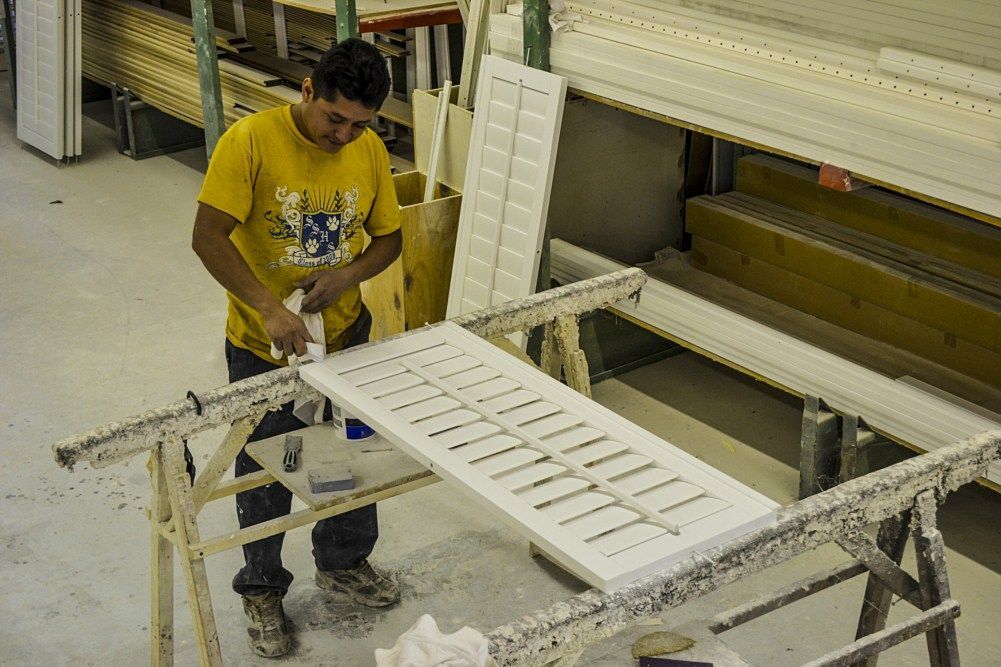 A man in a yellow shirt is working on a piece of wood.