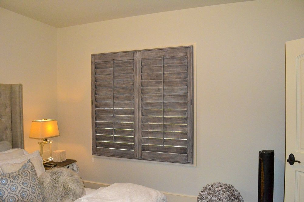A bedroom with a bed , lamp , and shutters on the wall.
